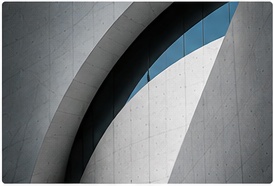 Curved concrete façade cutting across a pale blue sky
